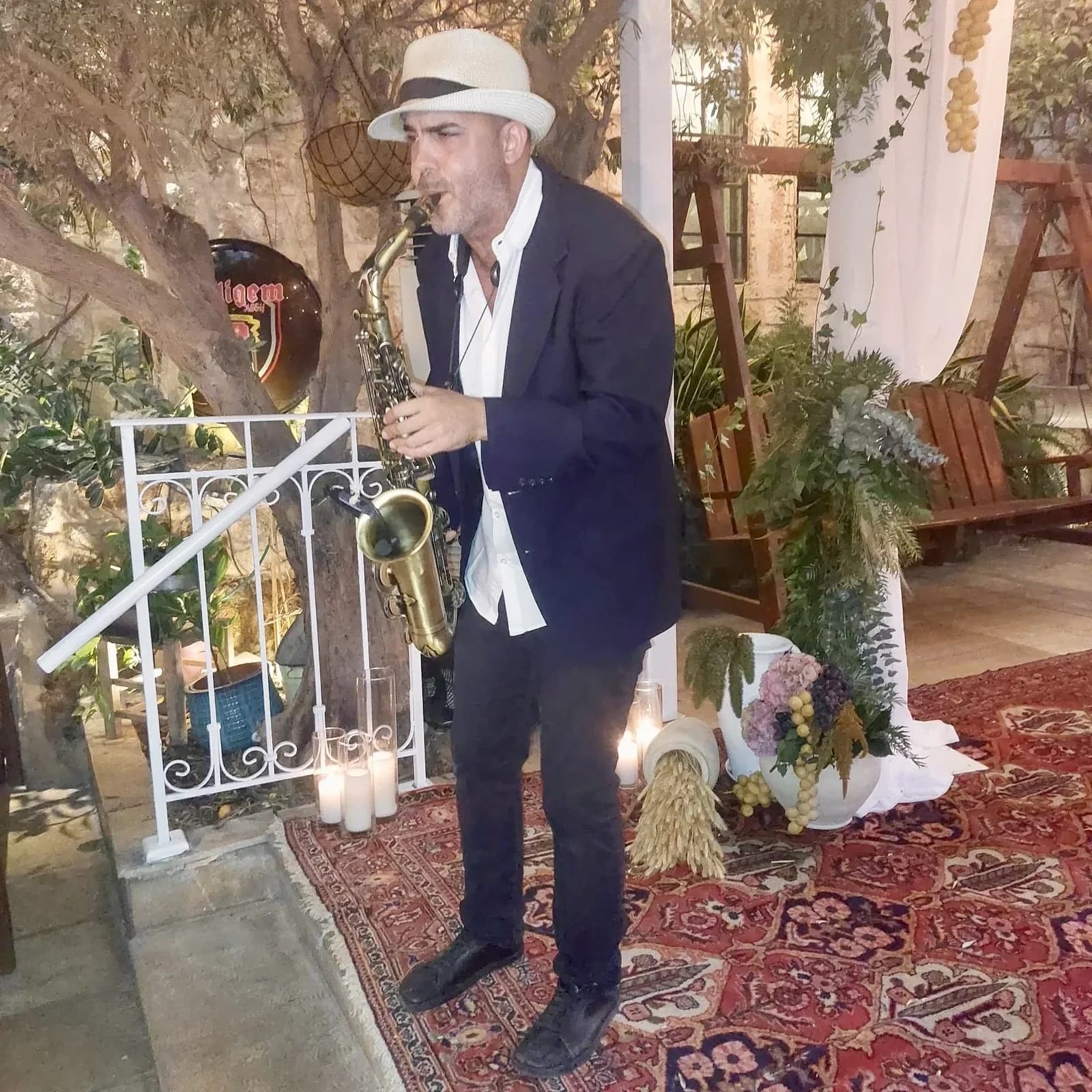 איתמר וגנר מנגן בסקסופון באירוע, בחליפה וכובע, לצד נרות ועיצוב פרחוני